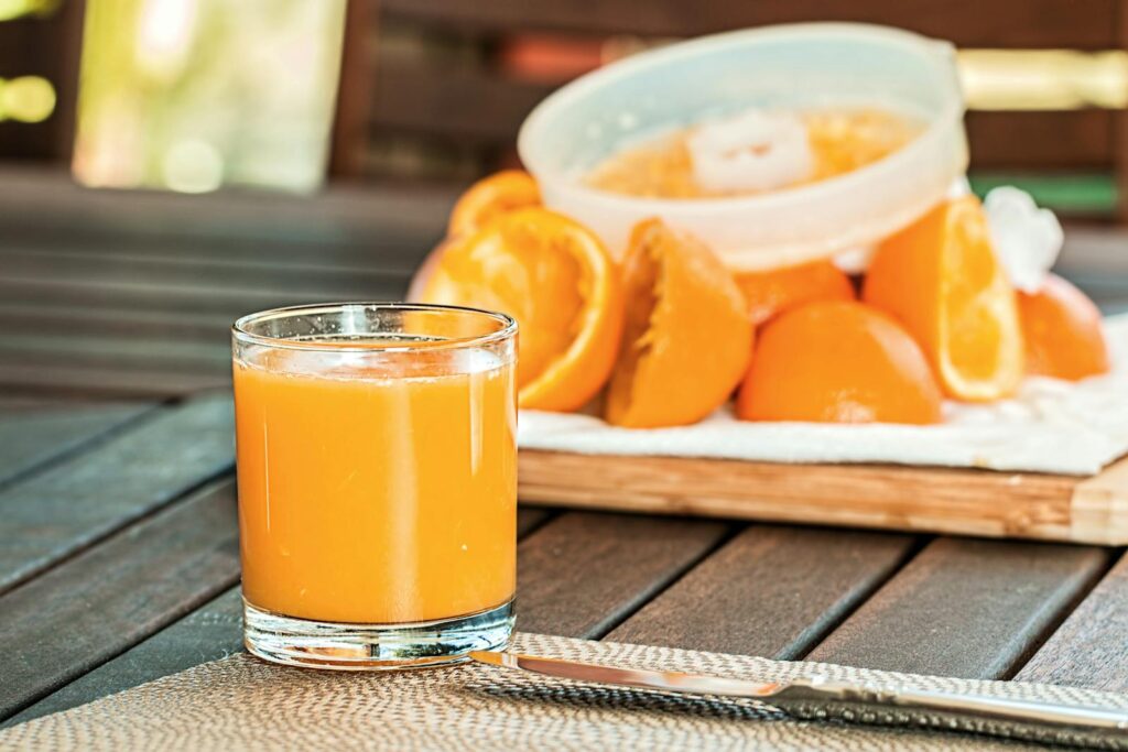 Glass of fresh orange juice with sliced oranges on wooden table, perfect for breakfast and healthy living.