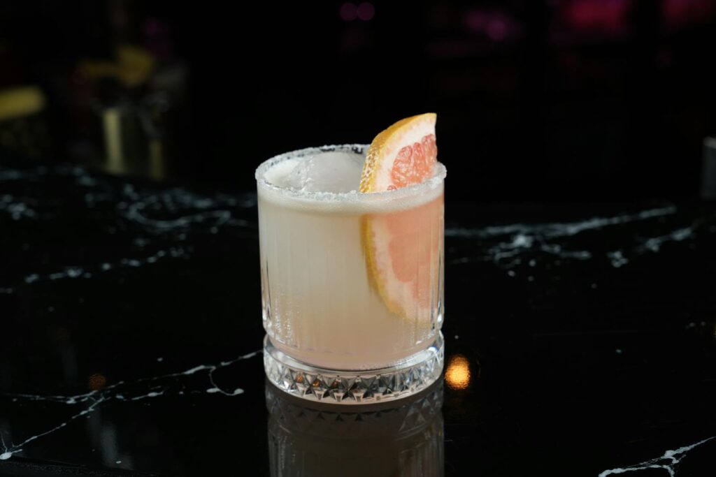 Elegant Paloma cocktail garnished with a grapefruit slice on a bar counter.