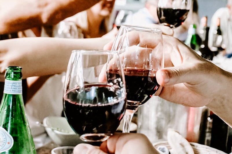 Celebrate with friends during a casual indoor gathering, raising glasses of red wine in a toast.