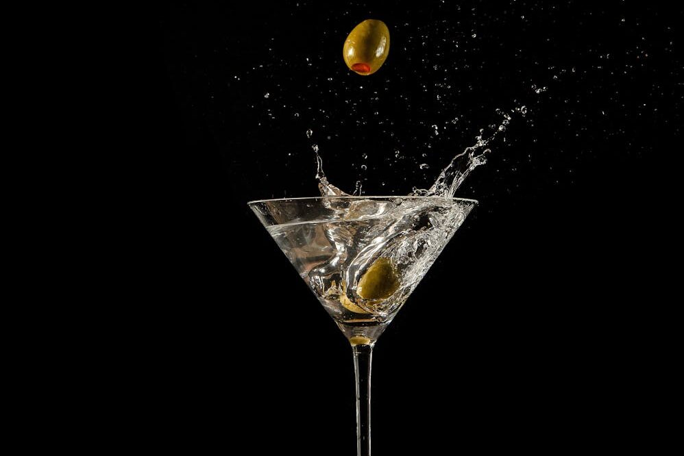 Martini glass with olives splashing against a black background, capturing motion and elegance.