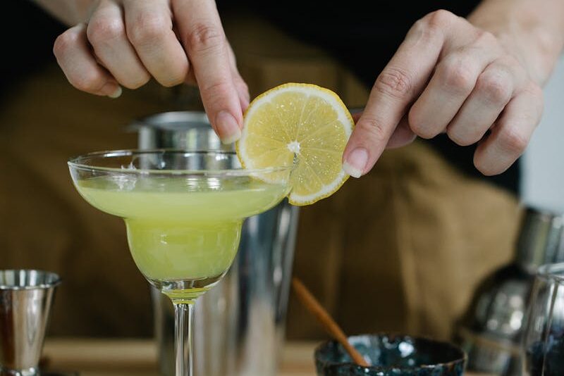 Close-up of hands preparing a fresh lemon margarita with garnish.