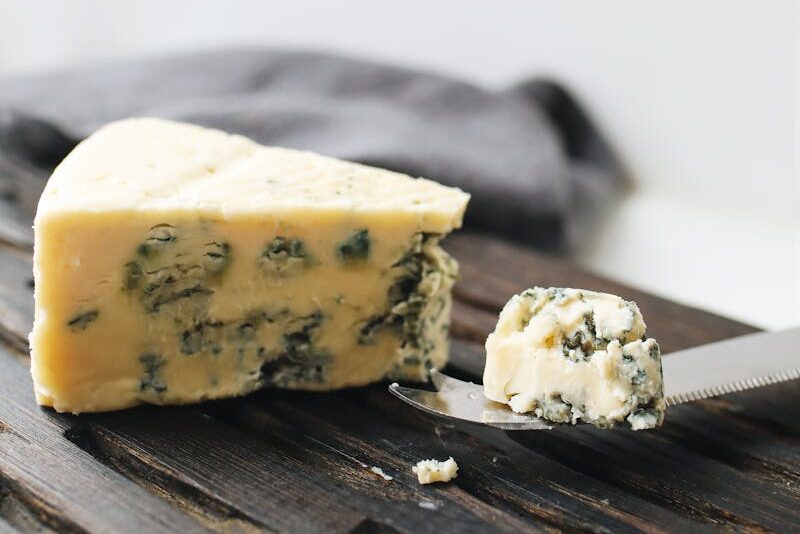 A detailed view of a wedge of blue cheese on a wooden surface with a knife.