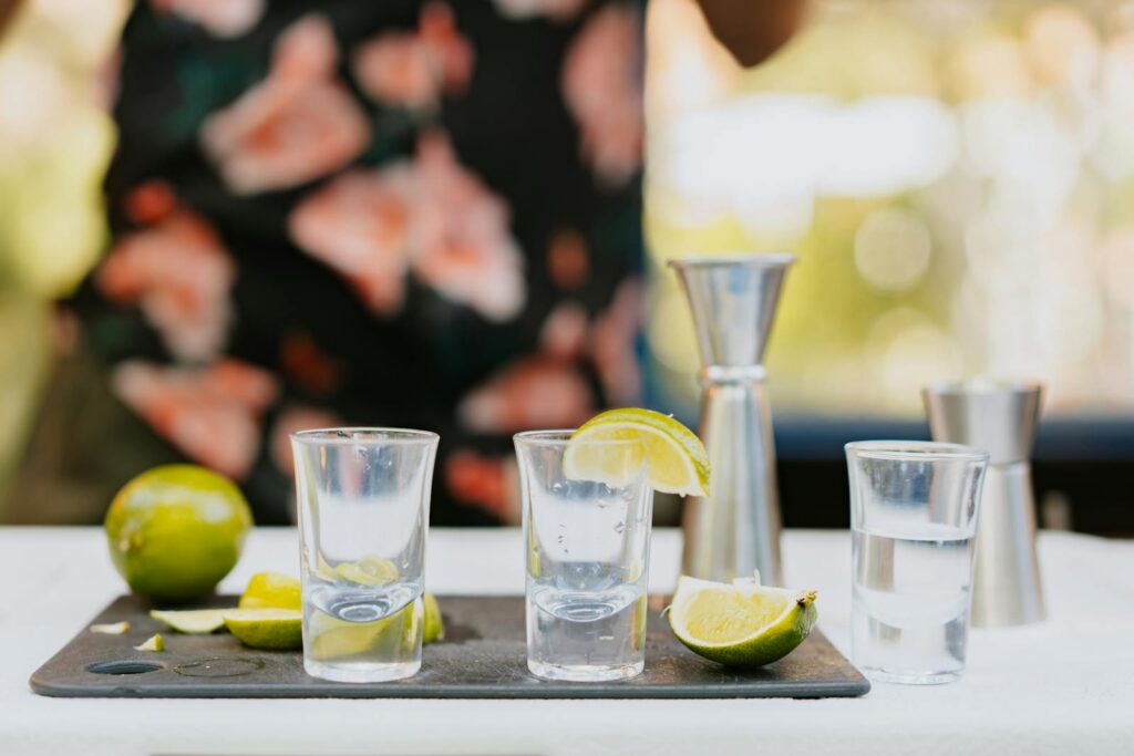 Close-up of shot glasses with lime slices on a summer day, with jiggers in the background.