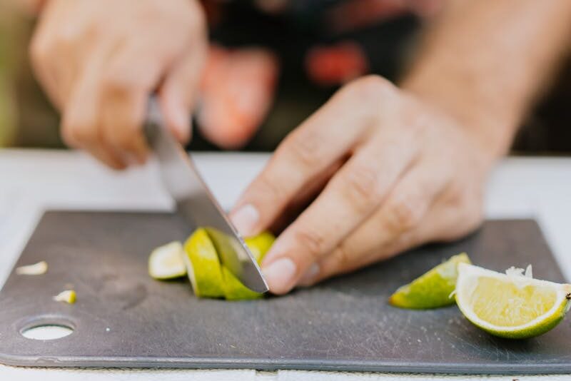 A person slicing fresh limes on a cutting board, focused on hands and knife.