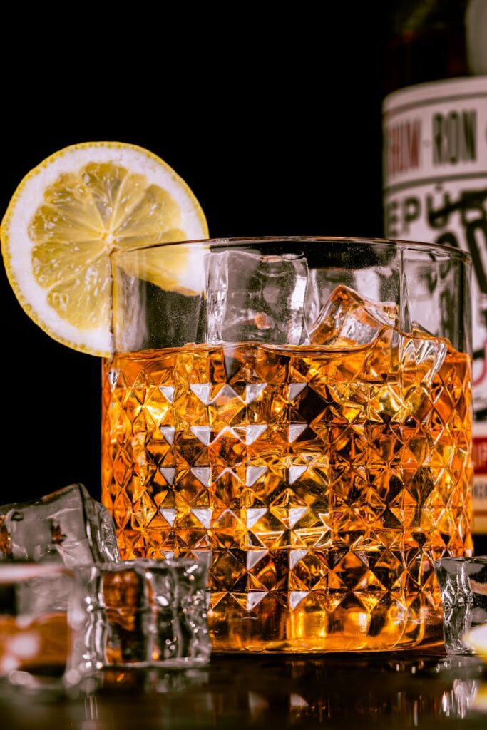 Close-up of whisky in a crystal glass with ice cubes and a lemon slice.