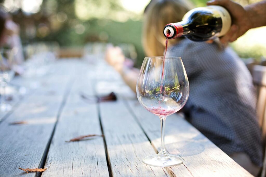 A hand pouring red wine into a glass on an outdoor table, creating a relaxed atmosphere.