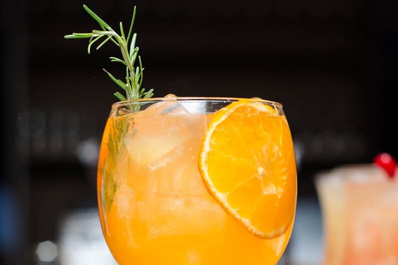 Refreshing orange cocktail with ice, garnished with rosemary and orange slice. Perfect for summer parties.