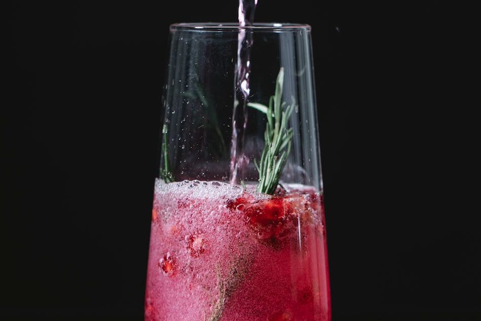 Crystal clean glass of red cocktail with berries and rosemary on black background