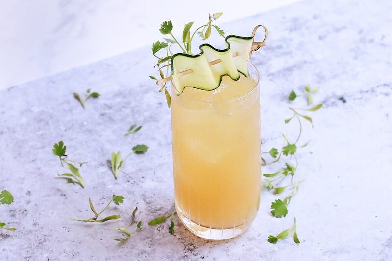 A refreshing citrus and herb mocktail with cucumber garnish on a marble table.