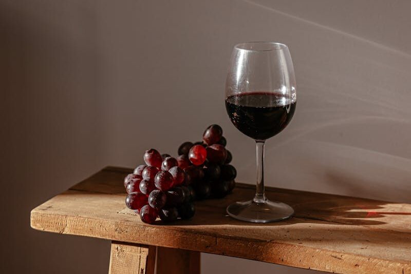 A sophisticated still life depicting red wine and fresh grapes on a wooden bench.