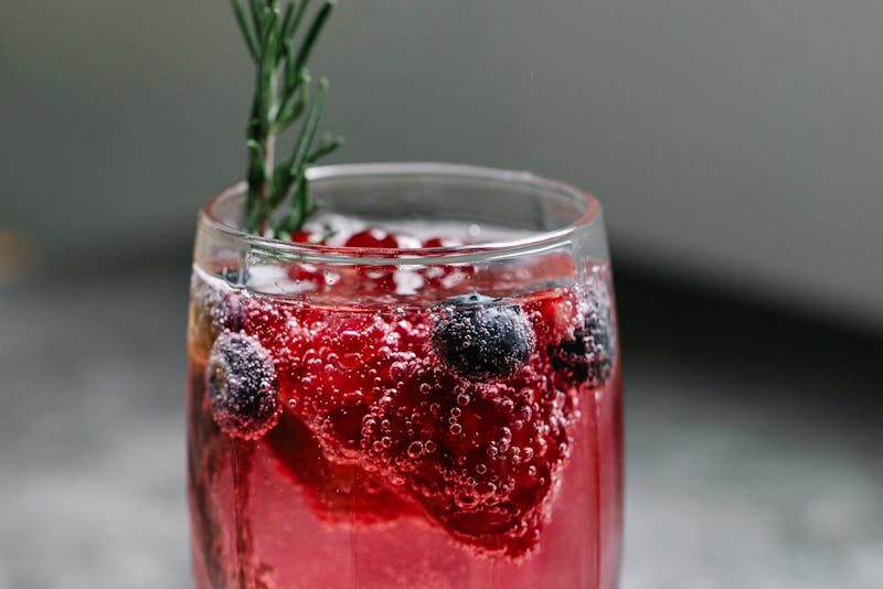 Close-up of a refreshing sparkling drink with berries and rosemary garnish in a glass.