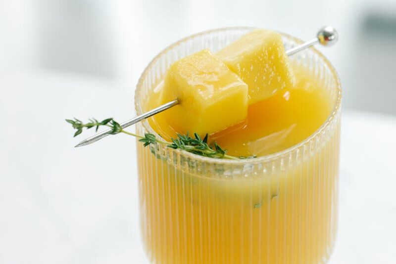 A refreshing pineapple cocktail with herb garnish served in a clear glass on a table.