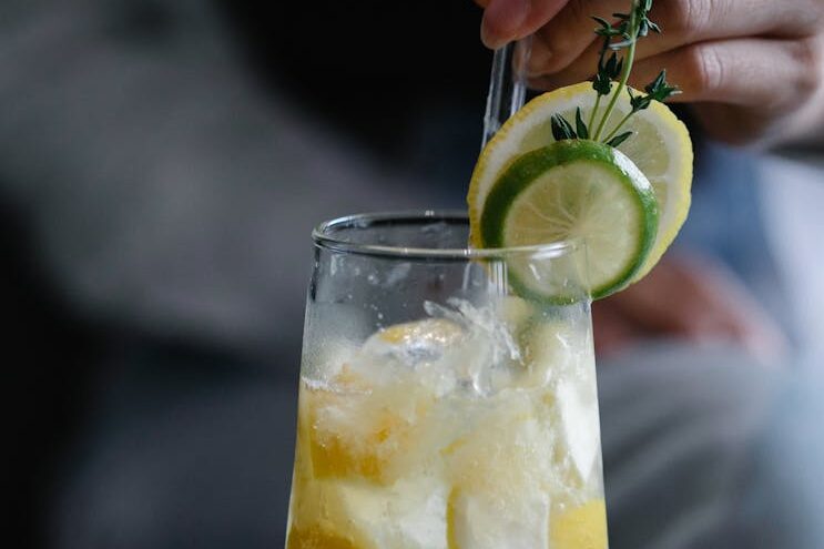 A chilled lemon lime cocktail with ice cubes in a glass, garnished with sprigs of herbs.