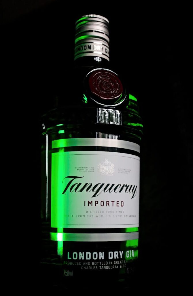 Close-up of Tanqueray gin bottle with striking green highlights against a dark background.